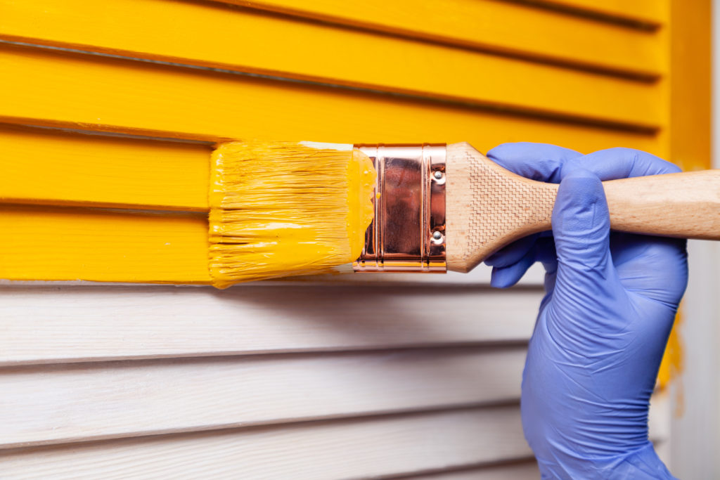 Woman painting the exterior of home with yellow paint.